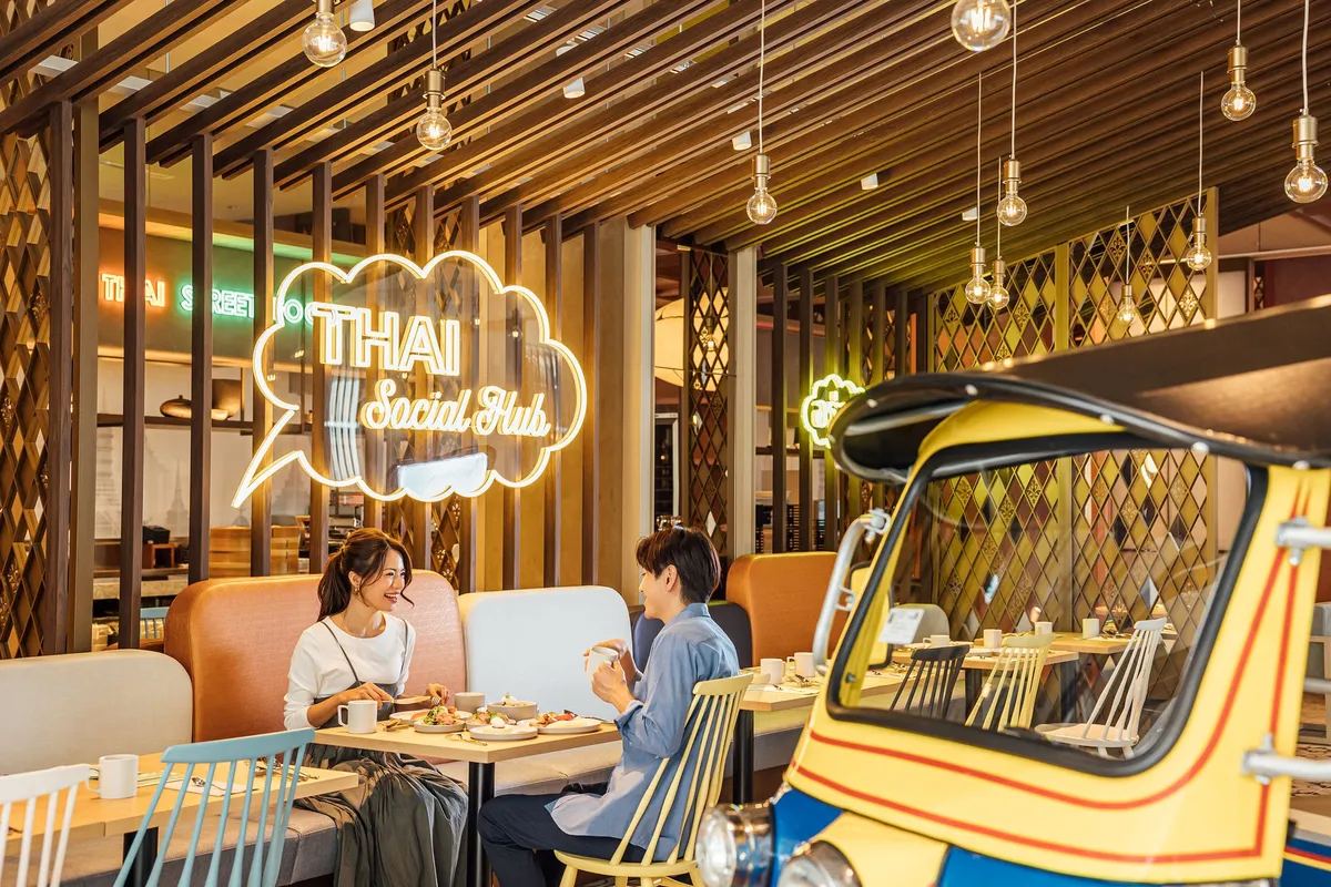 スアンブア店内でカップルが食事する様子。THAI Social Hub のネオンサインとトゥクトゥクを模したインテリアが映るレストラン内観写真