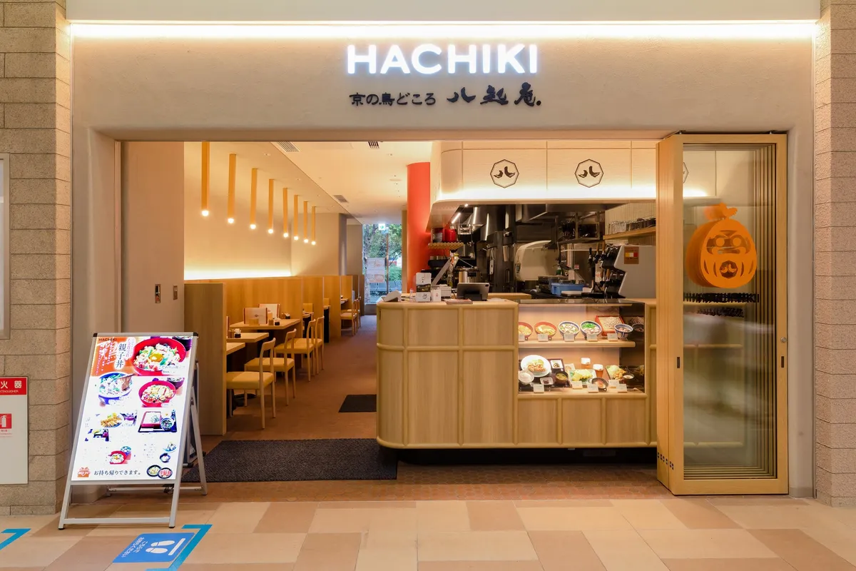 HACHIKI 八起庵の飲食店舗正面外観。店名看板・木調カウンター・食品サンプルケース・店内テーブル席・A看板(親子丼メニュー)が確認できる