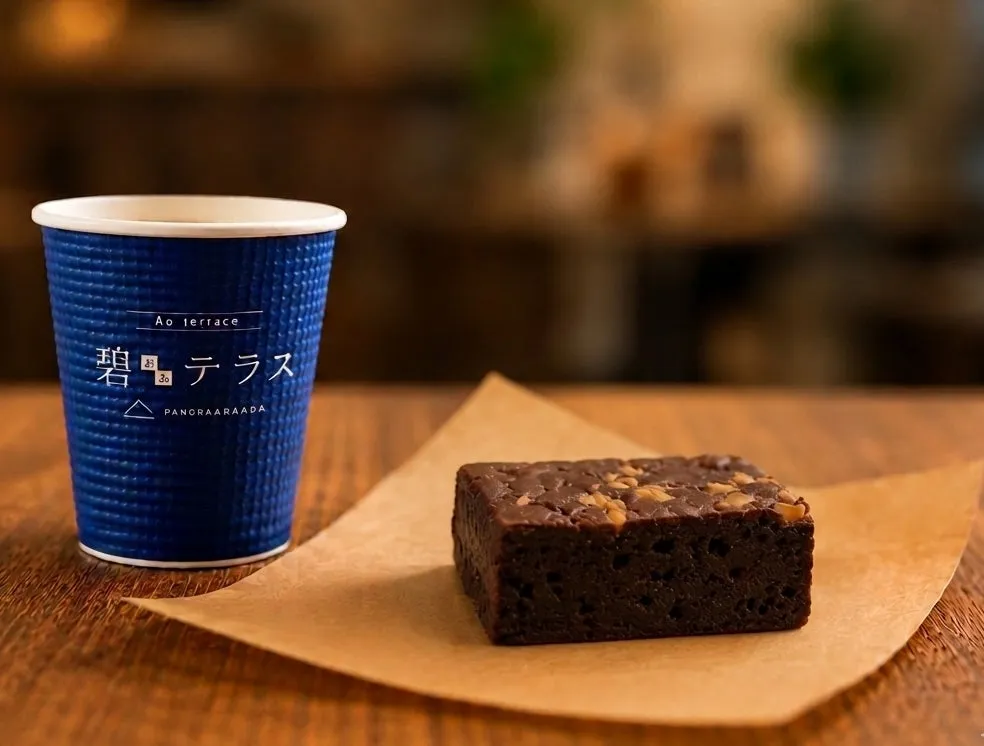 伊豆パノラマパーク碧テラスロゴ入り紙カップのコーヒーと、ナッツトッピングのチョコレートブラウニーをクラフト紙の上に並べたカフェメニュー商品写真