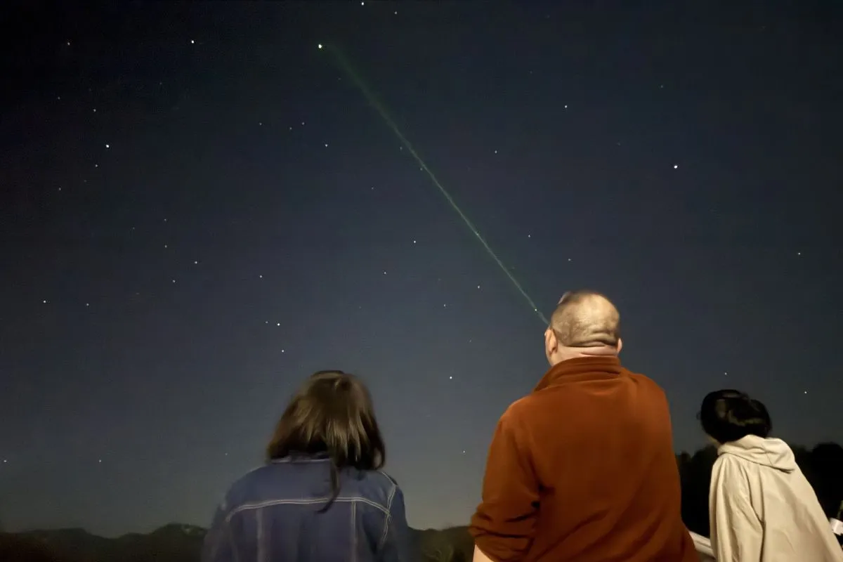 3人の参加者が屋外で夜空を見上げ、グリーンレーザーポインターで星座を指し示す星空観察体験のショット