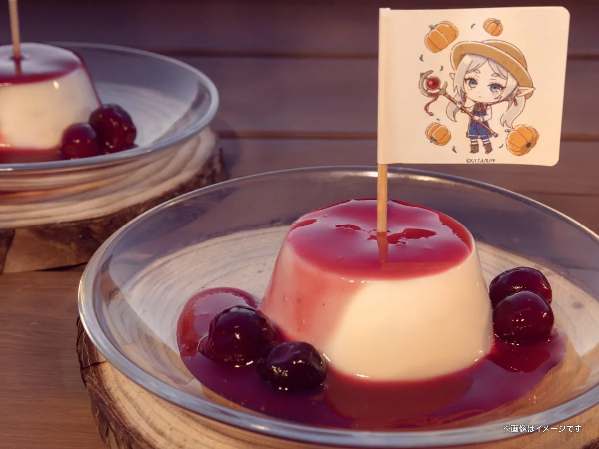 メルクーアプリン1個のクローズアップ。フリーレンの帽子と杖を持つちびキャラ旗を刺し、赤いソースとダークチェリーが皿に広がる近接カット。後方に同商品が1個ぼかしで写る