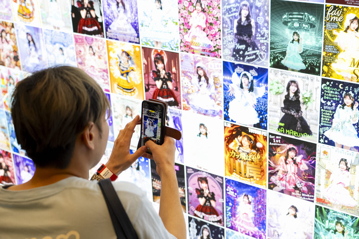 ファンの応募作品500件のうち選抜分が壁面いっぱいに展示された「祝福ボード」前で記念撮影するファン