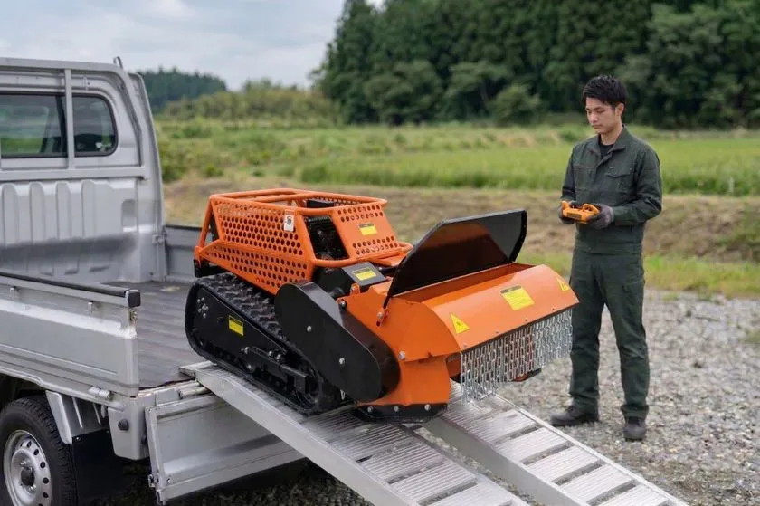 軽トラックのアルミスロープからJRY800を降ろす作業シーン。作業者がリモコンを手に持ち操作する様子と、屋外フィールドでの輸送・展開工程が確認できる