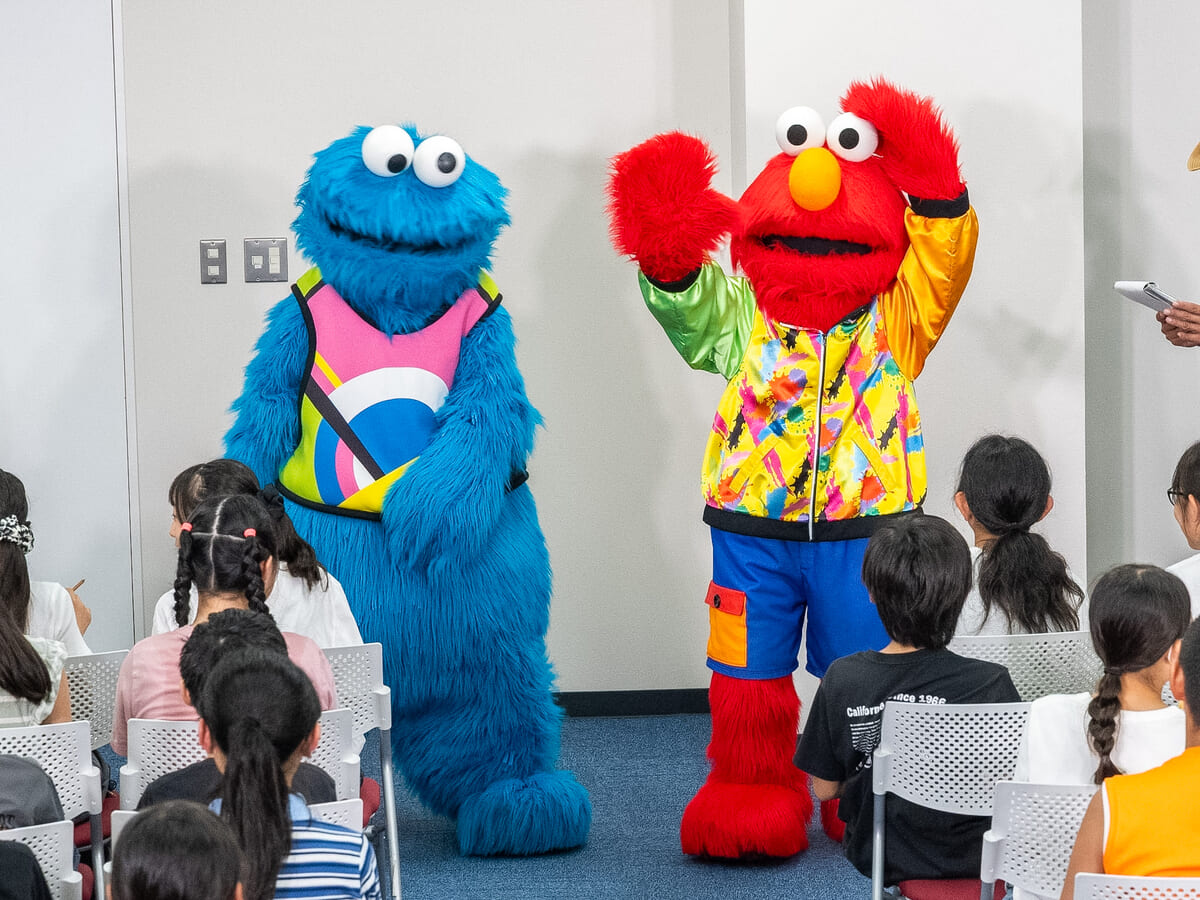 「クッキーモンスター」と「エルモ」が子どもたちに手を振る様子