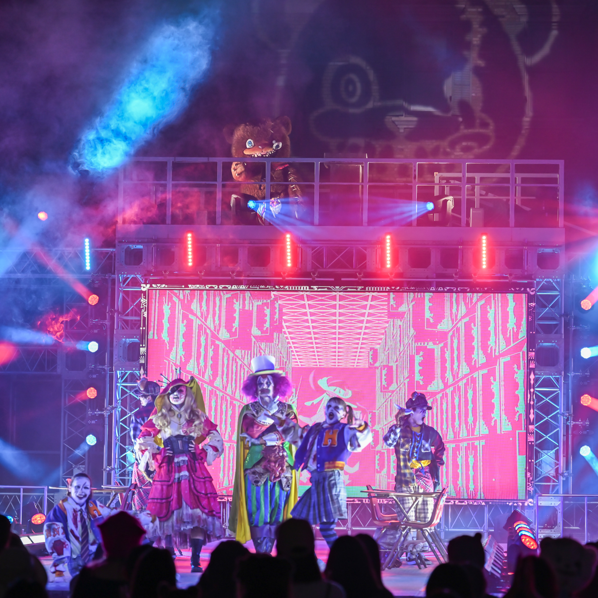 赤い映像スクリーンを背景に並ぶ出演者