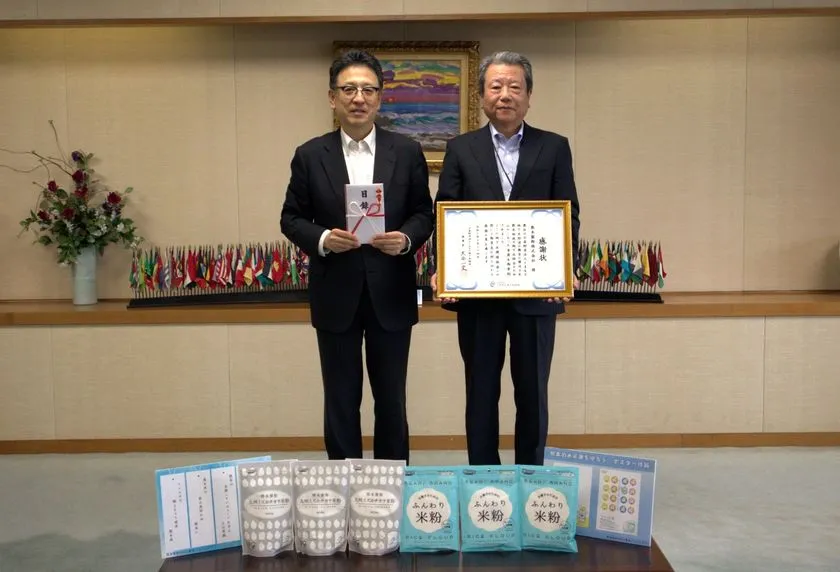熊本市役所の庁議室で、寄付目録と感謝状を手にした2名が米粉製品を前に並んでいる寄付贈呈式の写真