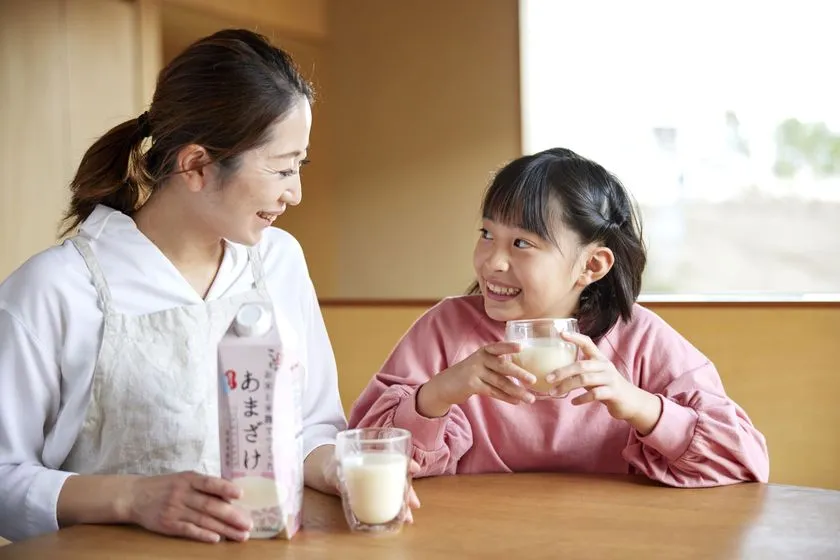 親子とみられる女性と子どもがテーブルで甘酒をグラスに入れて飲んでいる飲用シーン