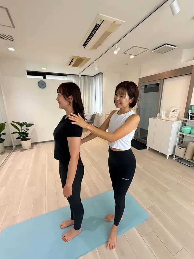 白を基調としたスタジオで、インストラクターが立っている女性の肩付近に手を添え