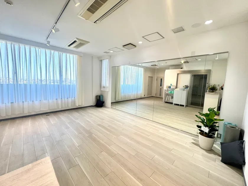 大きな窓と壁一面の鏡を備えた、白と淡い木目で統一されたピラティススタジオの室内