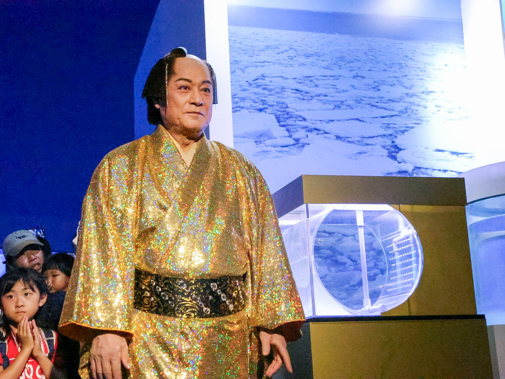 アクアミュージアムの展示前に立つ金の着物姿の松平健さん