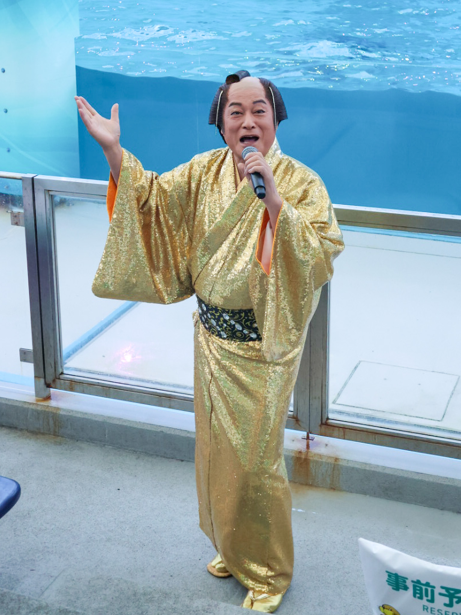 プールを背にマイクを手に語りかける金の着物姿の松平健さん