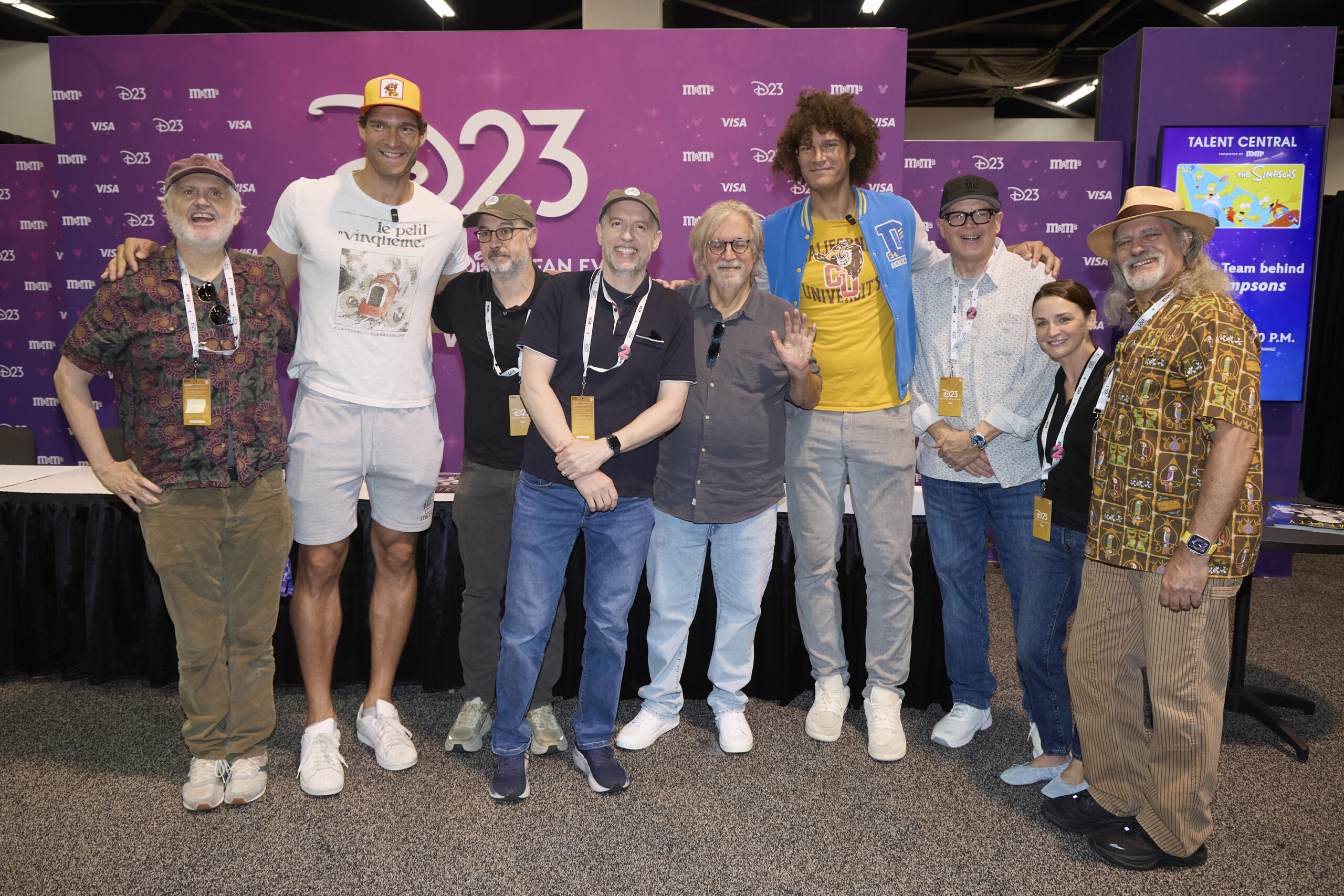 D23のバックドロップ前に並ぶ『ザ・シンプソンズ』のキャストと制作陣9人の集合写真