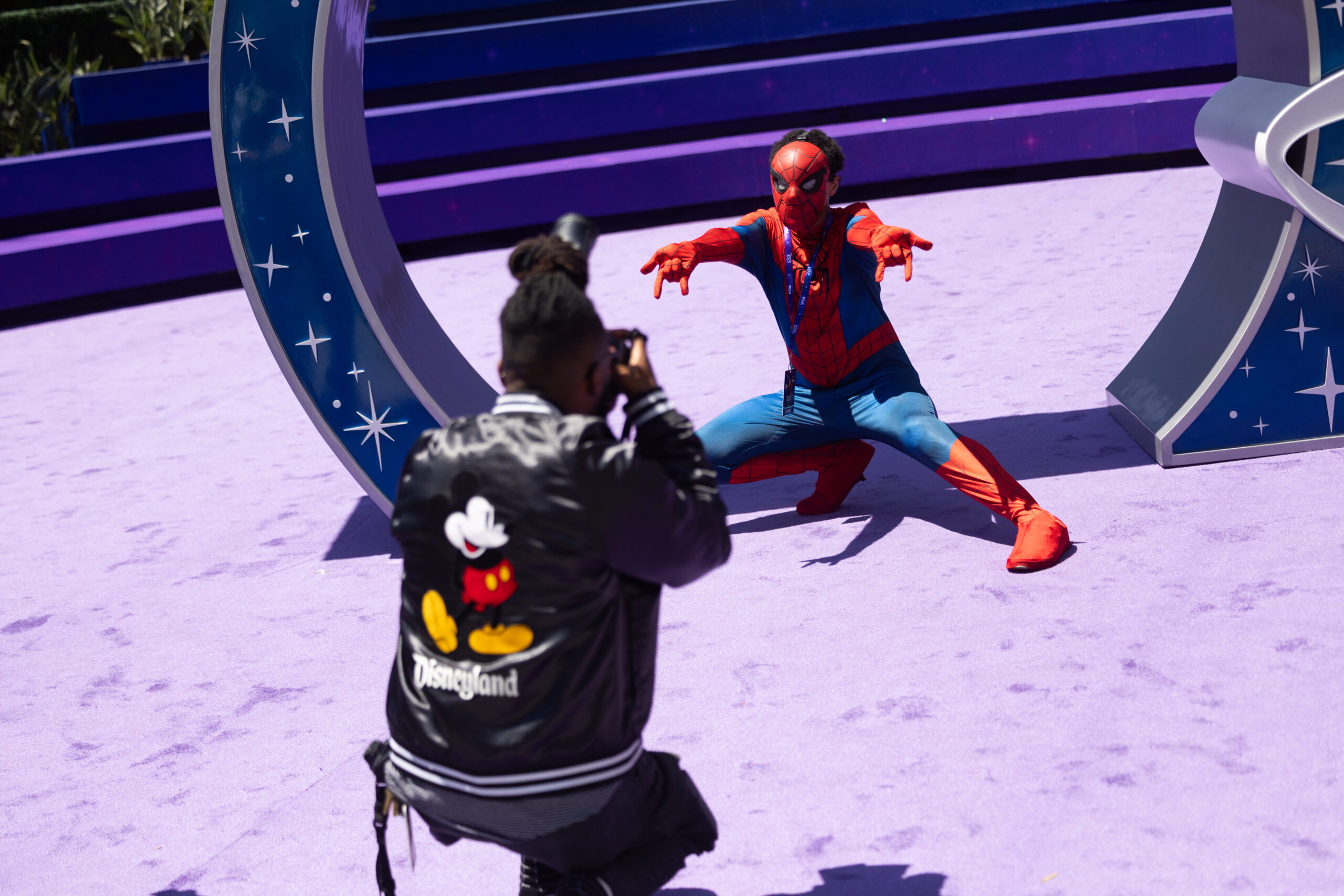 D23サインの前で腕を広げるスパイダーマンと、それを撮影する来場者