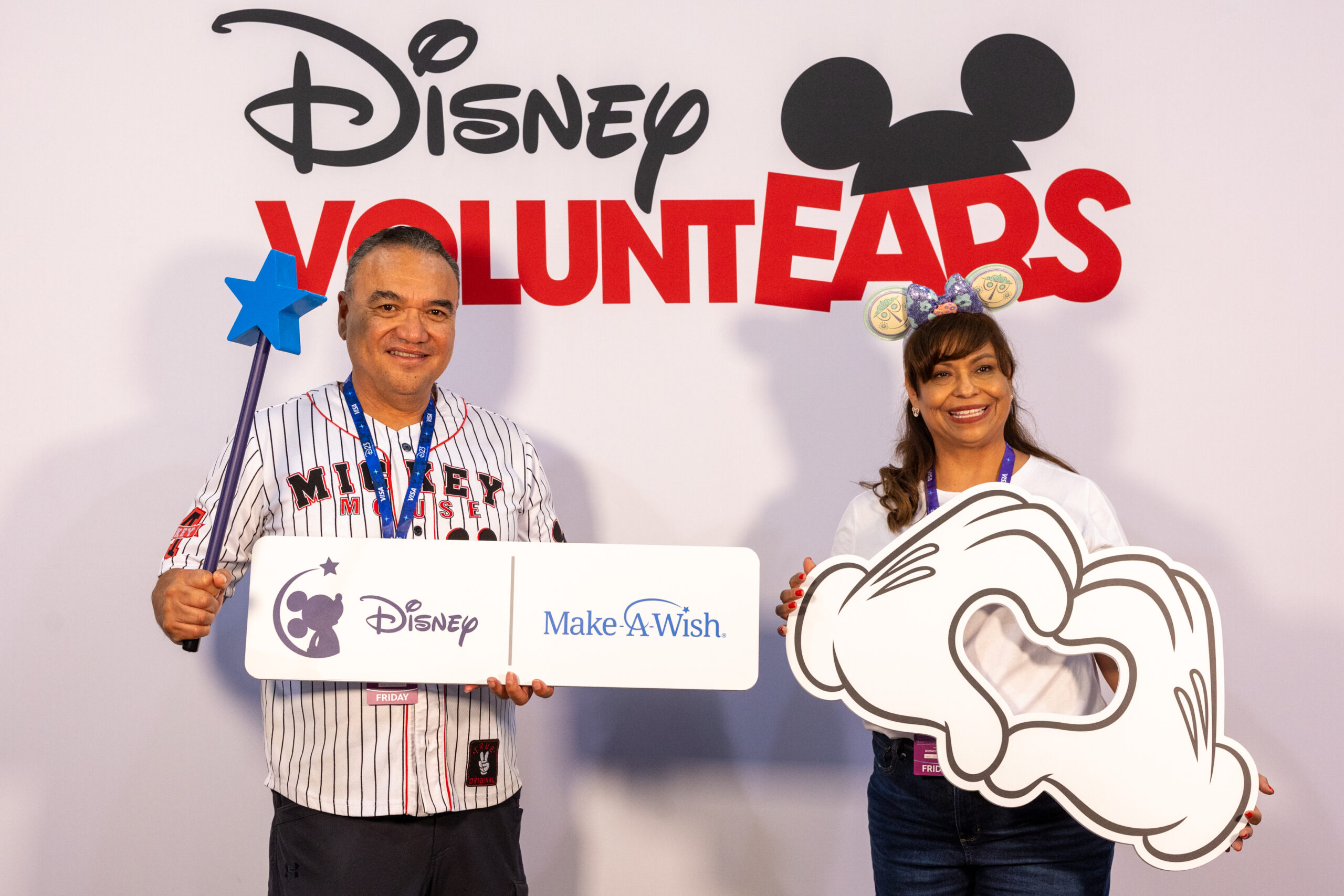 Disney VOLUNTEARSのバックドロップの前でDisneyとMake-A-Wishのロゴが入ったプラカードを持つ来場者