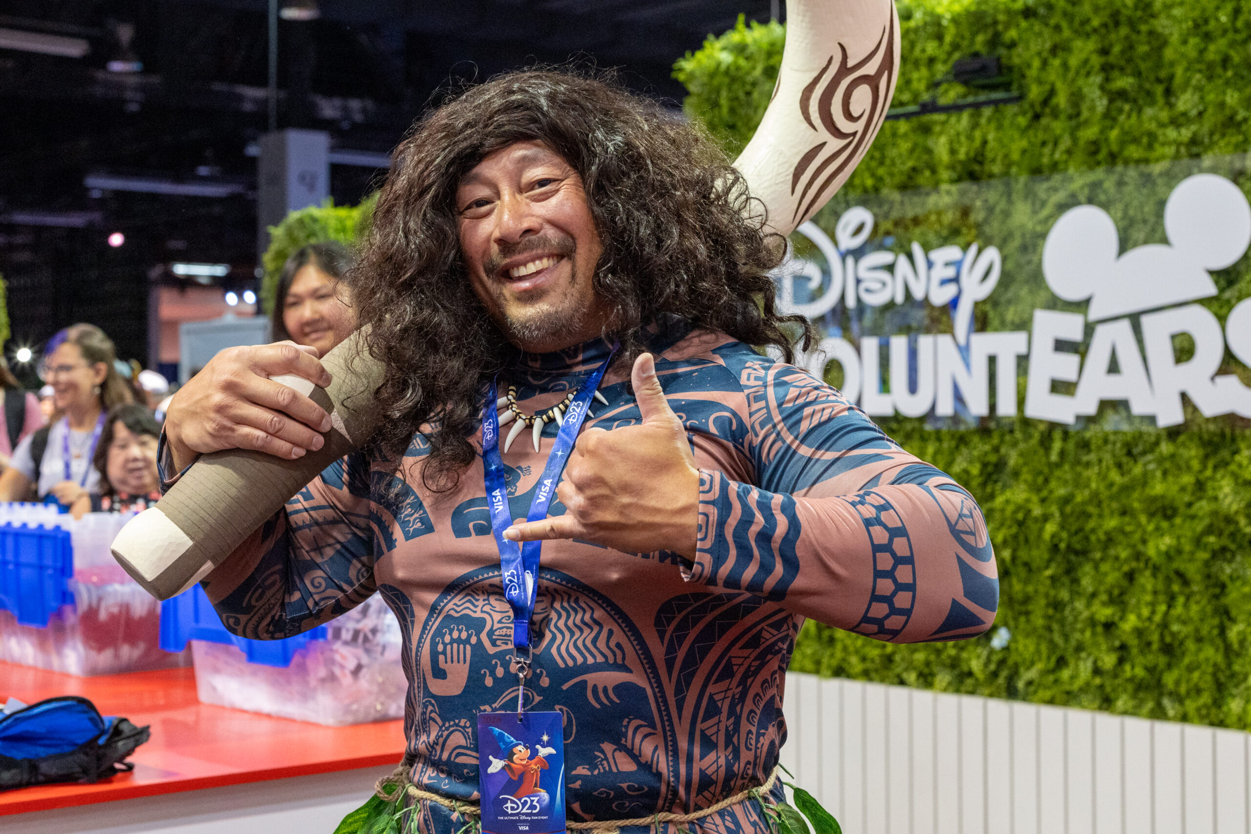 Disney VOLUNTEARSのロゴを背に釣り針のプロップを担いだマウイのコスプレ姿の来場者