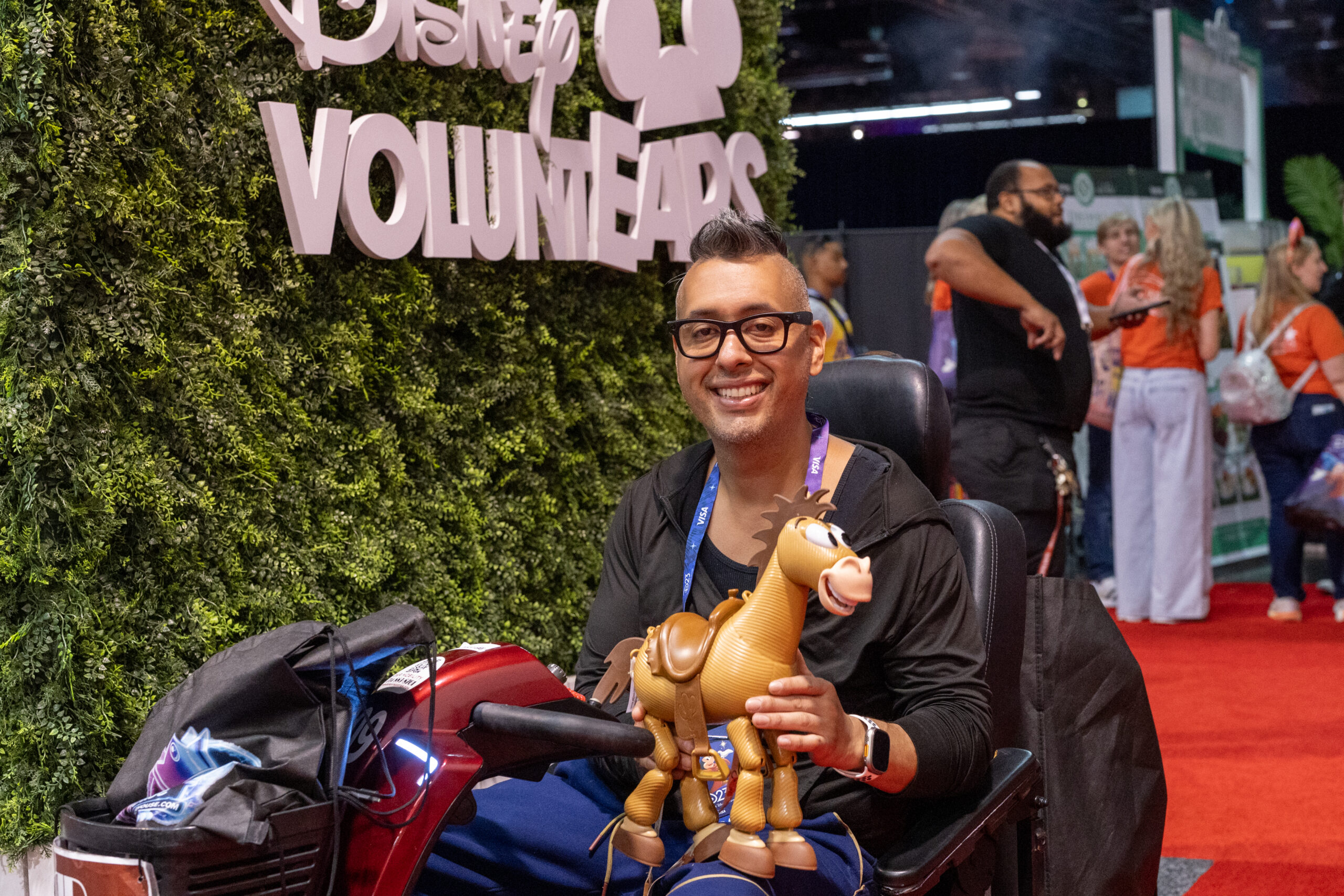 Disney VOLUNTEARSの植栽壁の前でトイ・ストーリーのブルズアイのフィギュアを持つ来場者