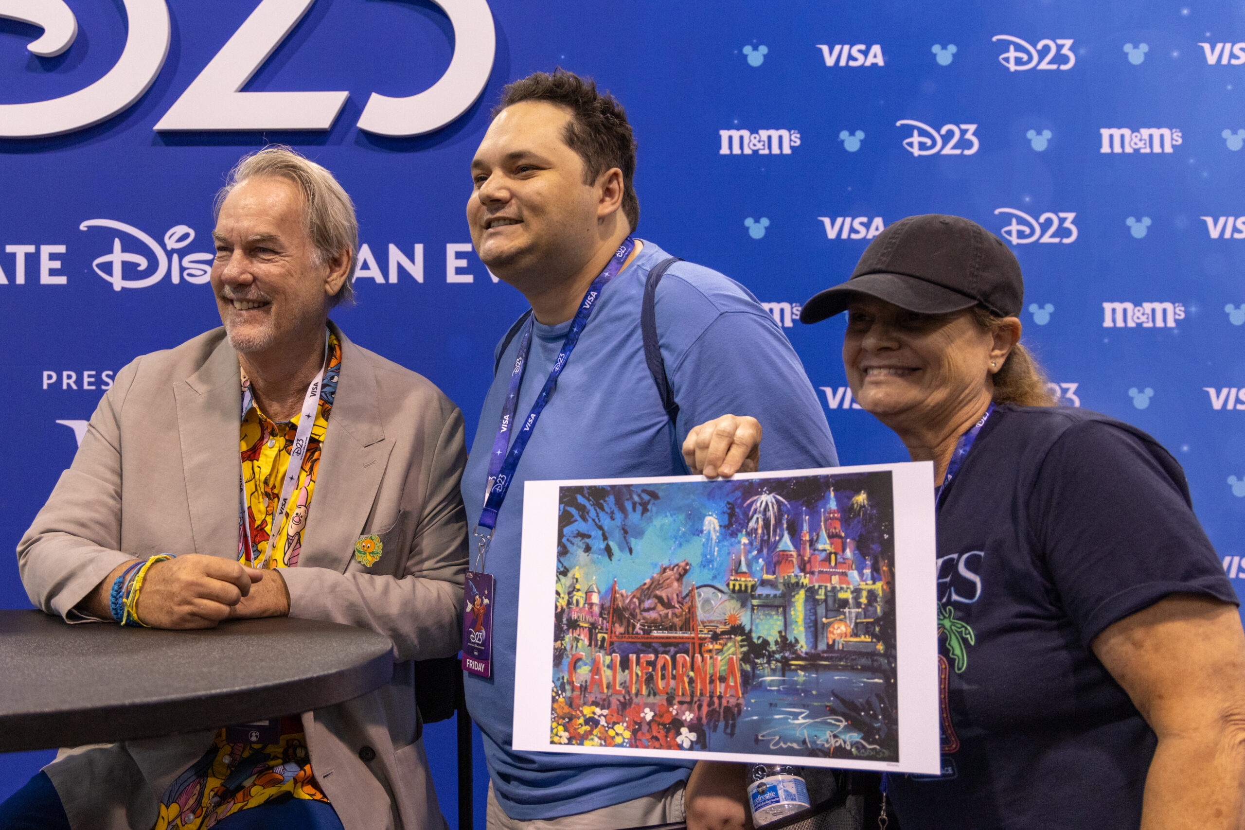 サイン入りの「CALIFORNIA」の印刷物を掲げる来場者2人と、テーブルに着くエリック・ロビソン