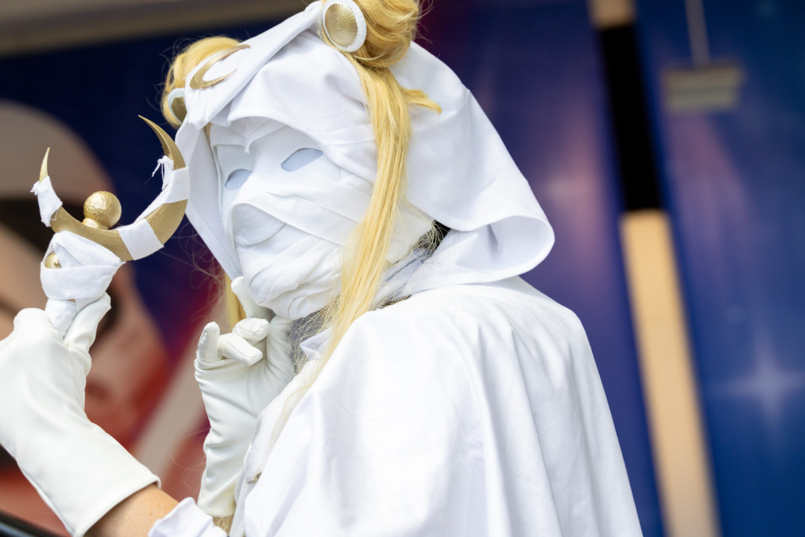 白い布で顔を覆い、金色の三日月型の杖を掲げるムーンナイトのコスプレイヤー