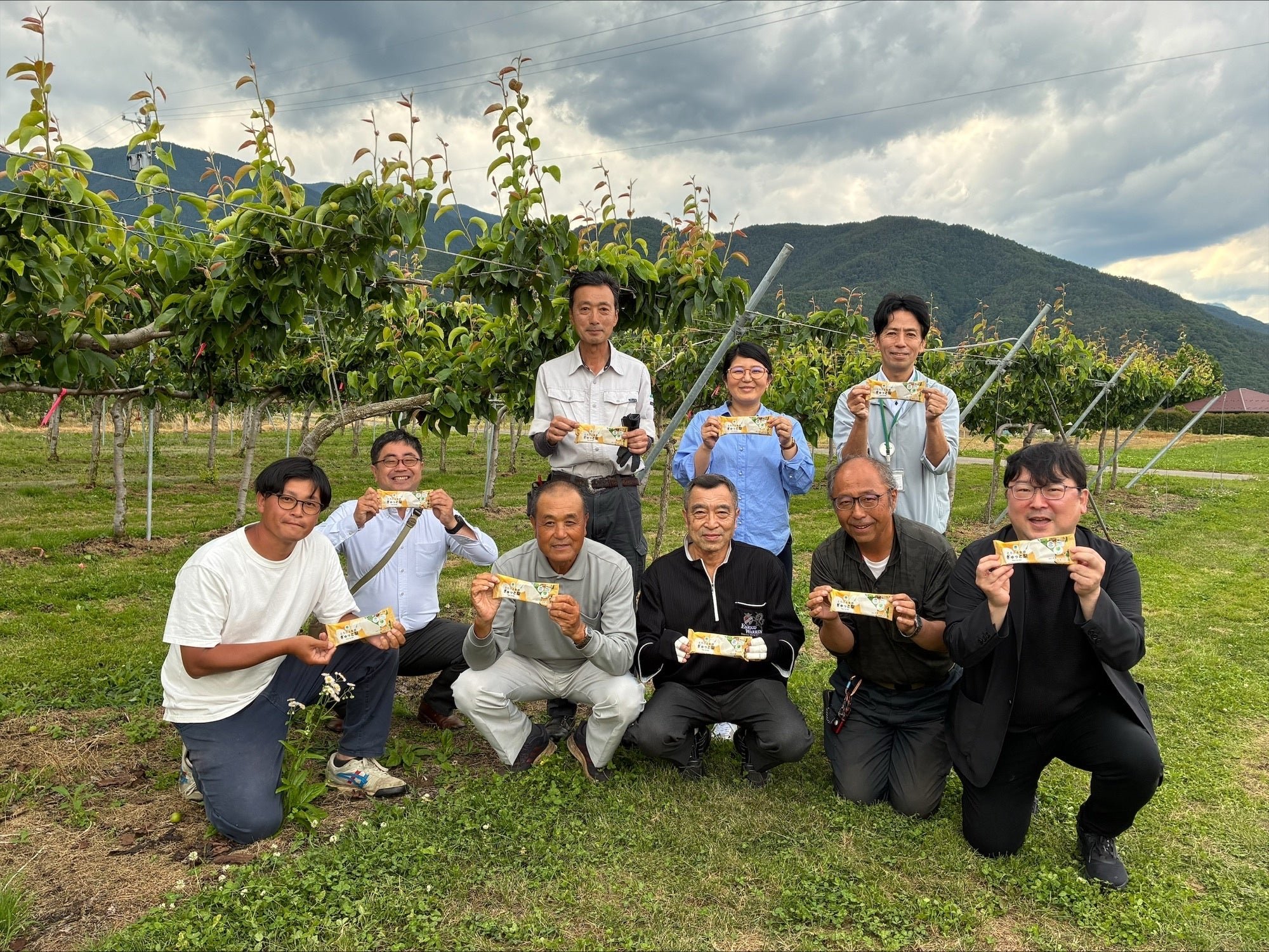 梨園で梨を胸元に掲げる農家のみなさん9人