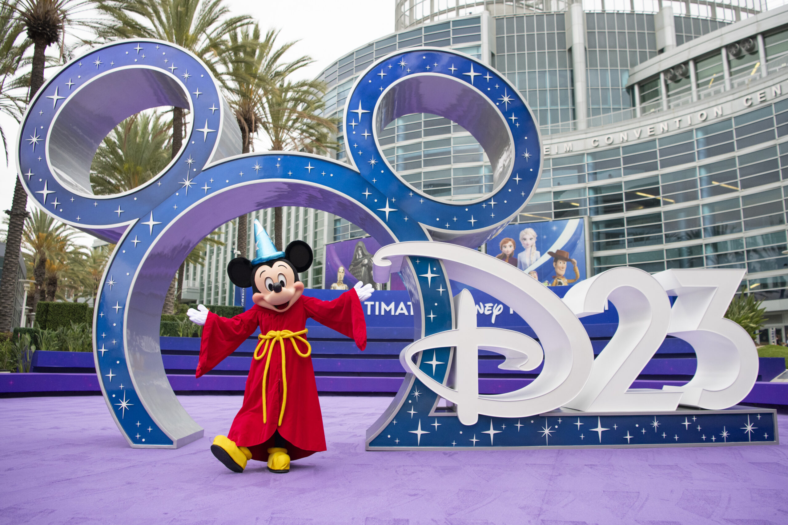 アナハイム・コンベンションセンター前のD23の巨大ロゴオブジェの前でポーズをとるソーサラー・ミッキー