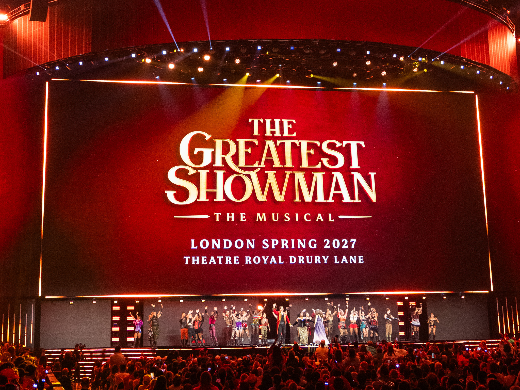 手を挙げて客席の歓声に応えるThe Greatest Showmanのカンパニー