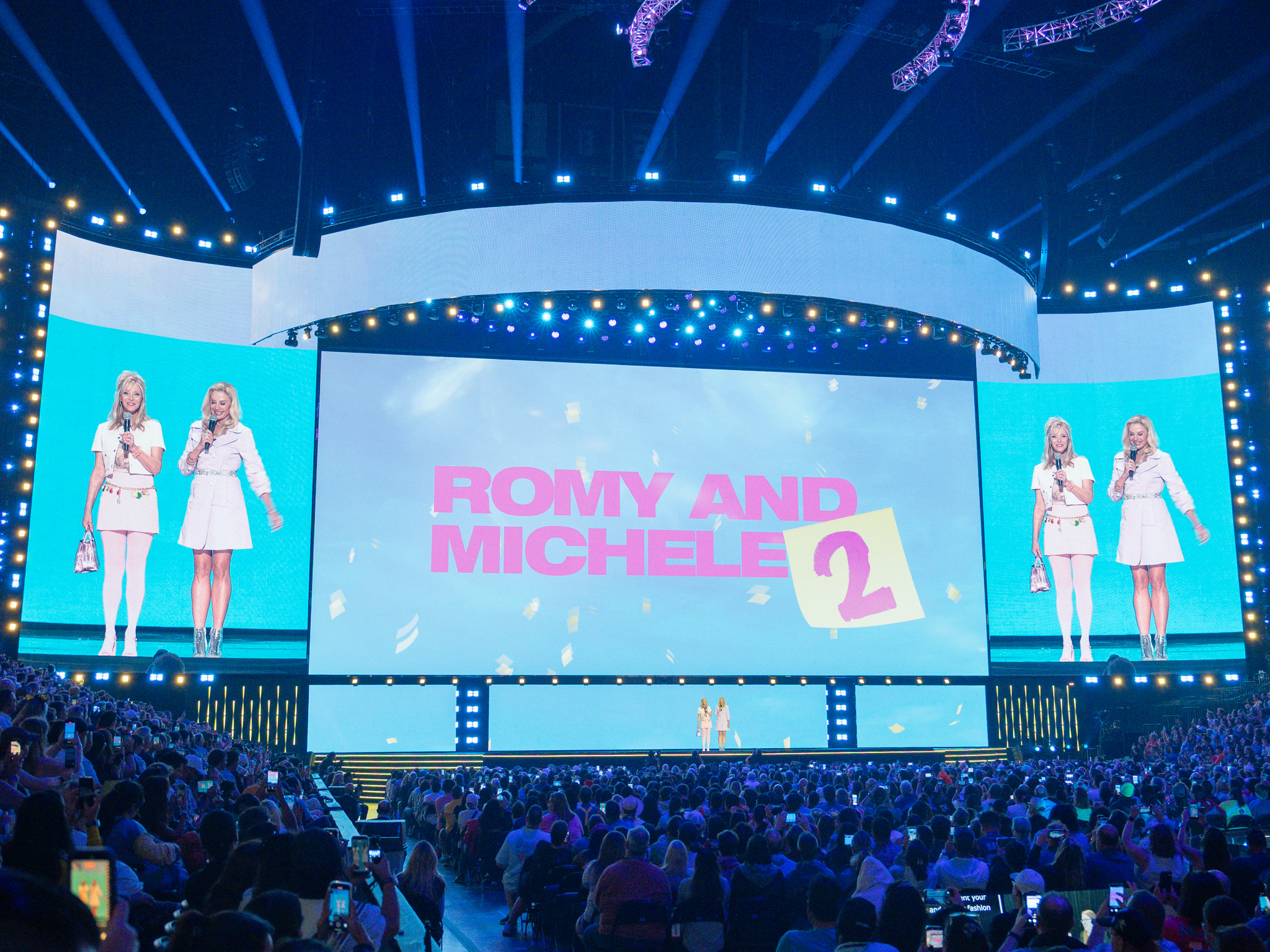 ROMY AND MICHELE 2のロゴが映るステージに立つ白い装いのリサ・クドローとミラ・ソルヴィーノ