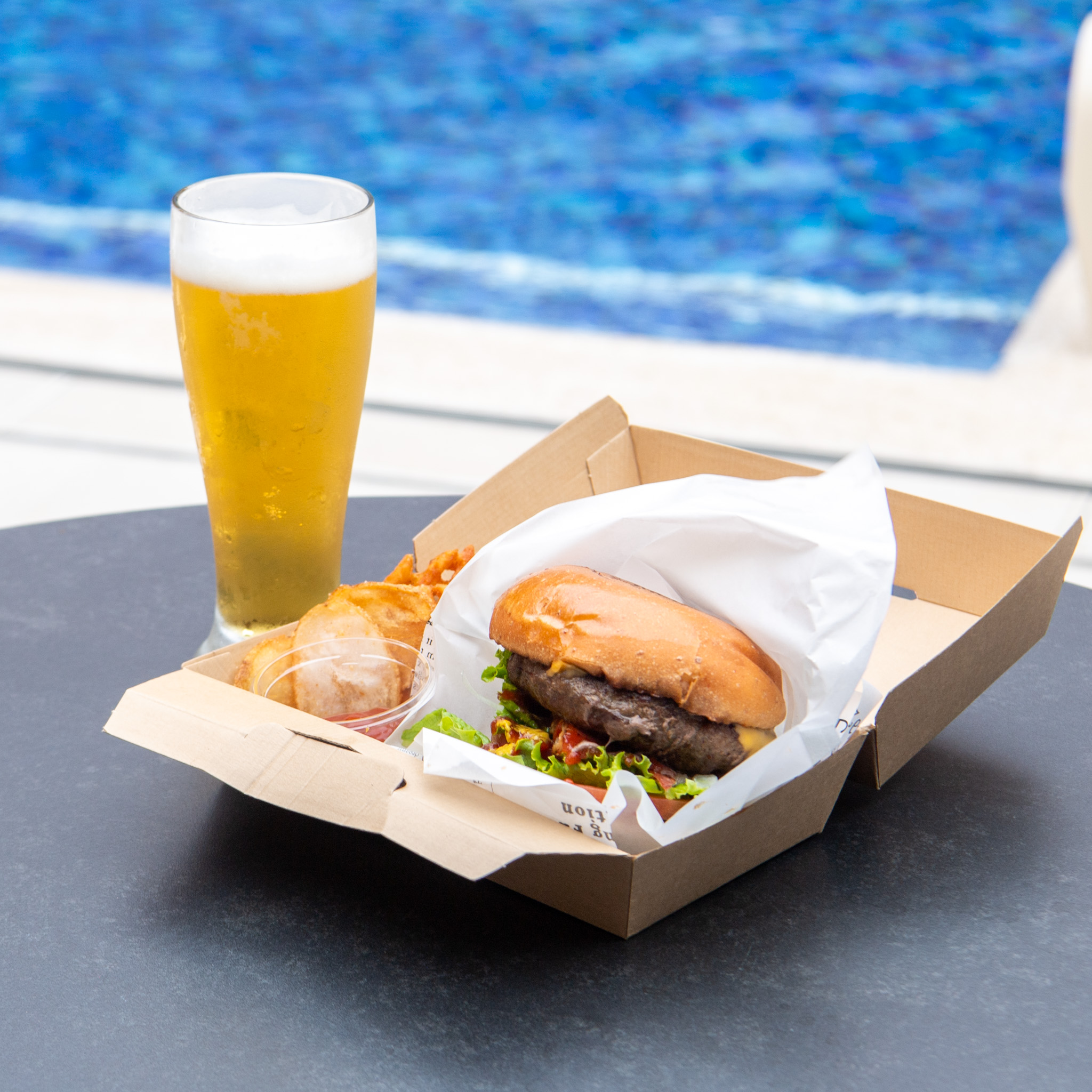 プールを望むテーブルに置いたハンバーガーと生ビール