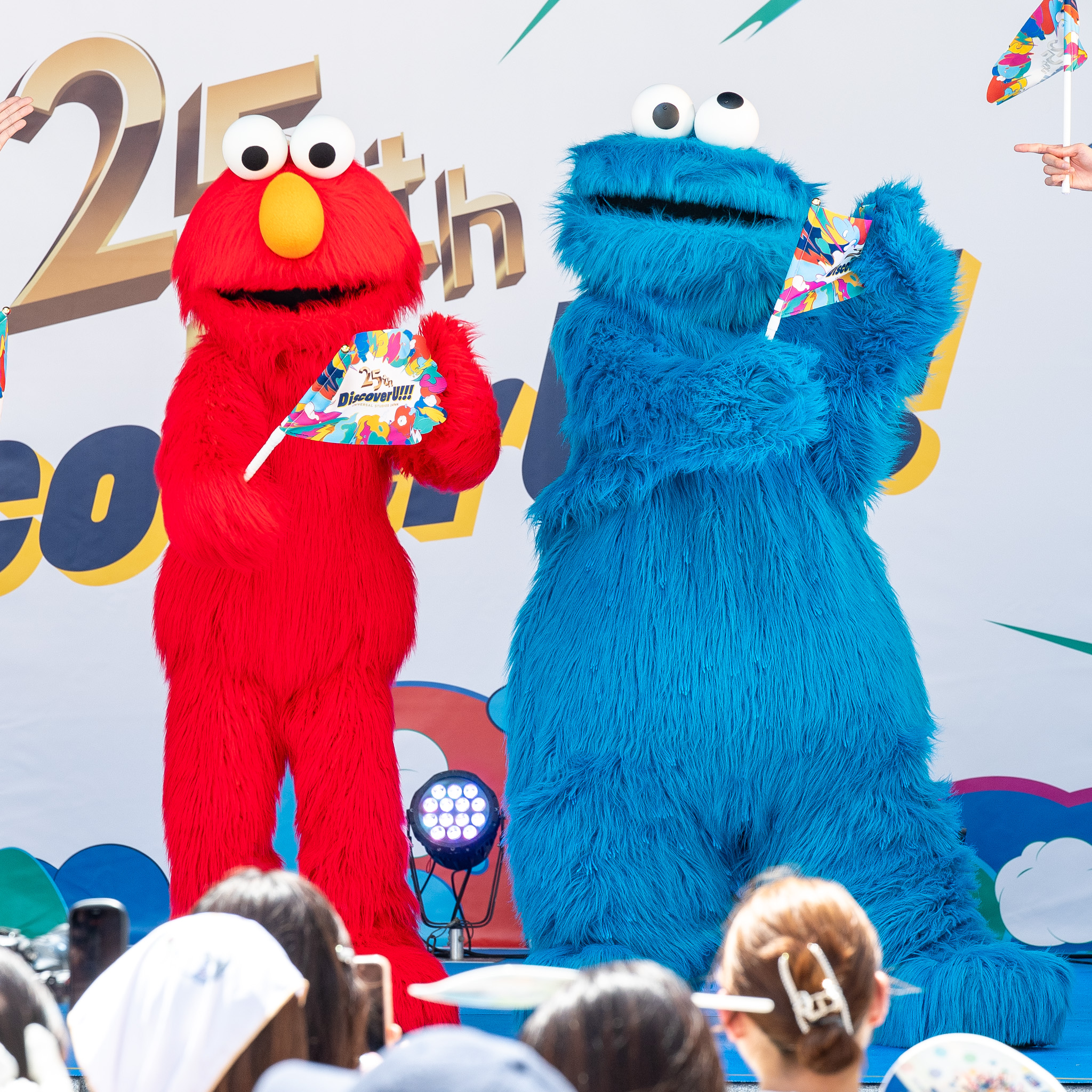 「25th Discover U!!!」の小旗を持つエルモとクッキーモンスター