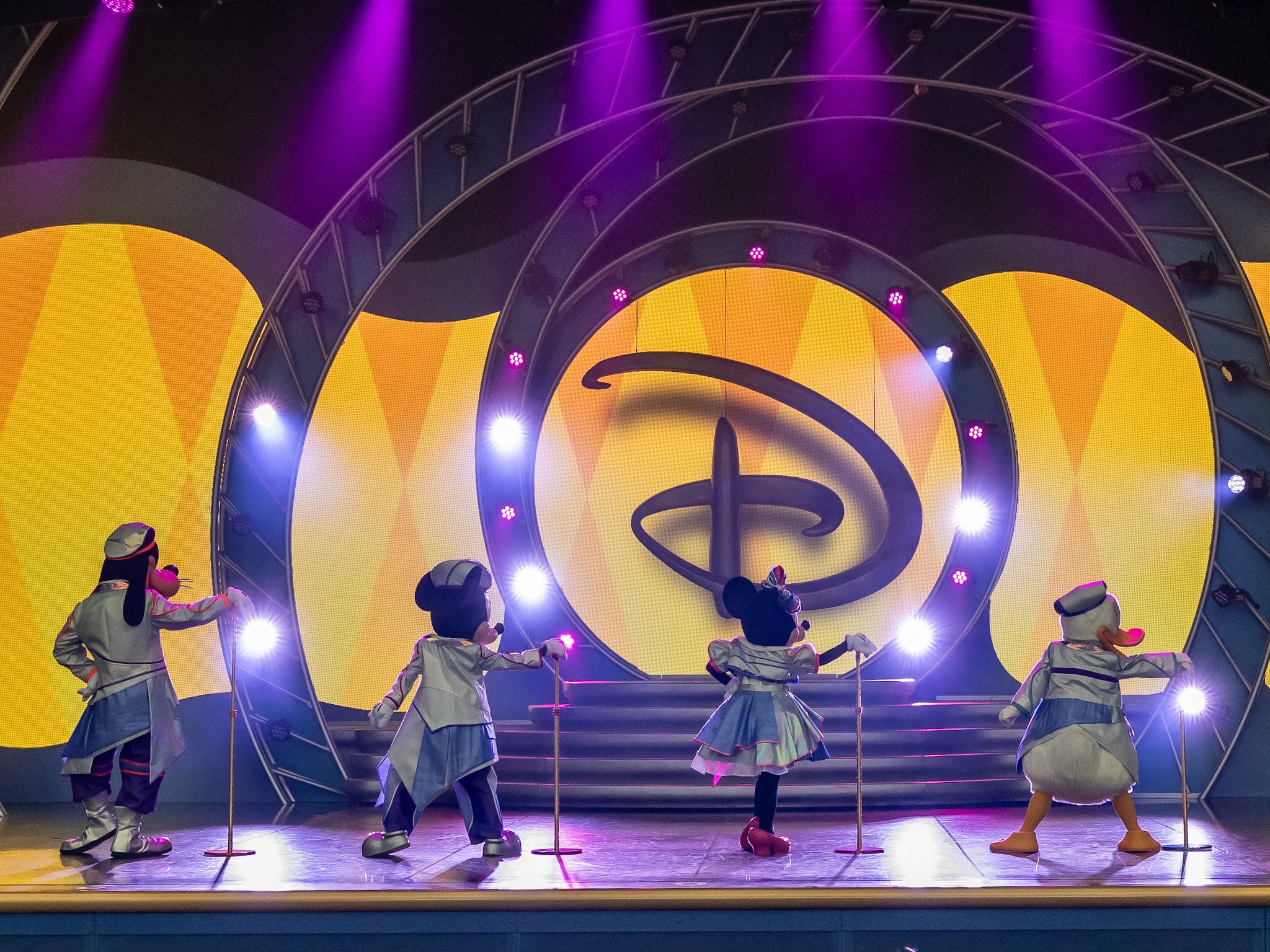 『It’s a Small World』の場面で光る円形のセットの前に立つディズニーの仲間たち