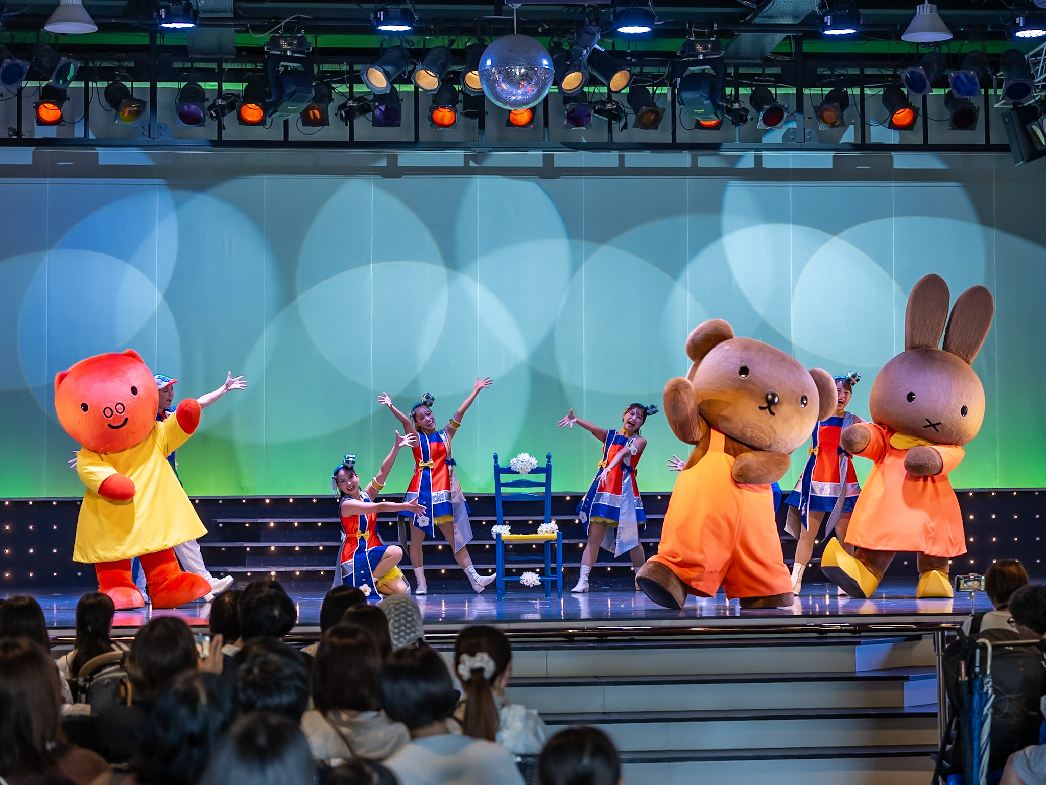 白い花を飾った青い椅子を囲んで踊るグランティ、ボリス、メラニー