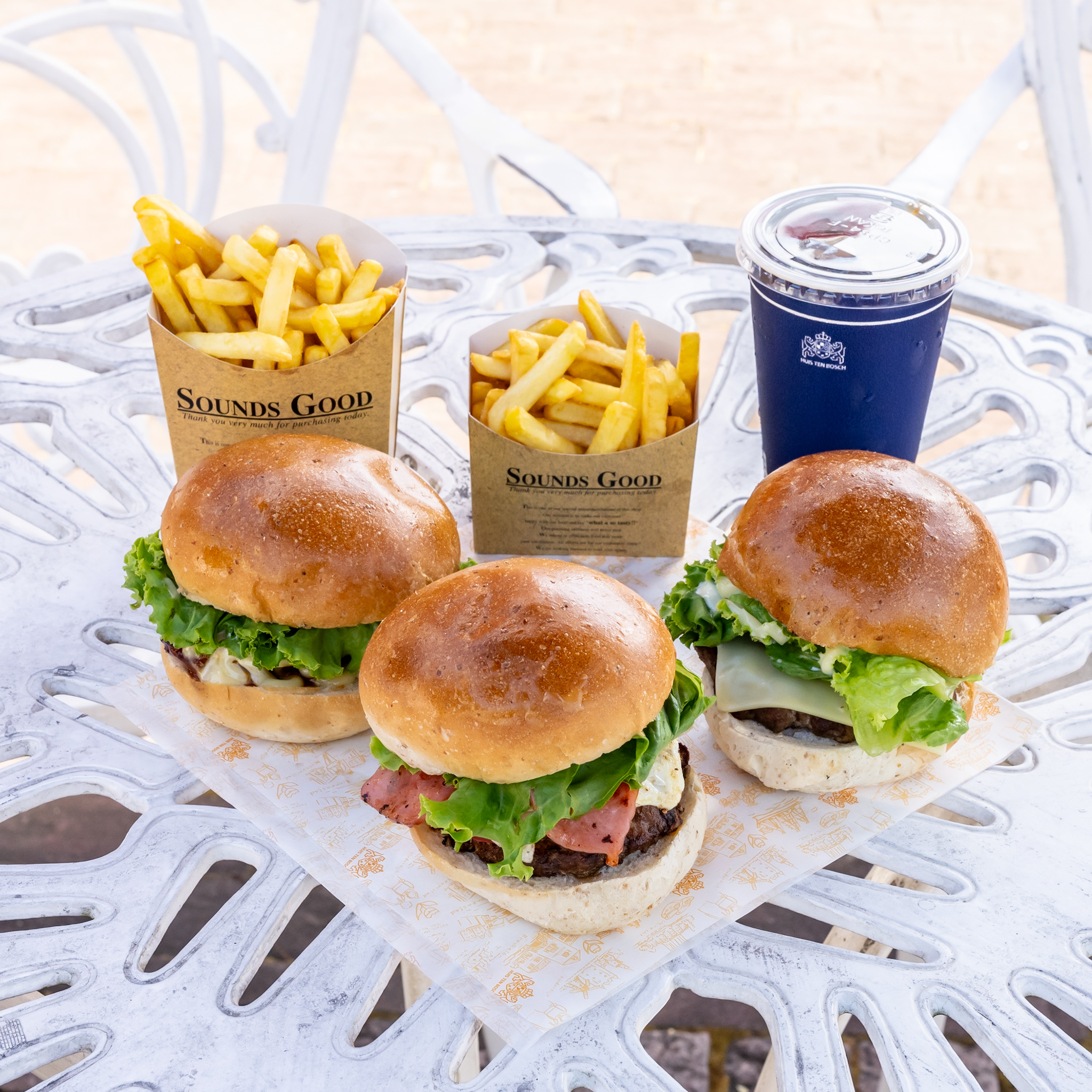 3種のバーガーとフライドポテト、ドリンクが並ぶテラス席のテーブル