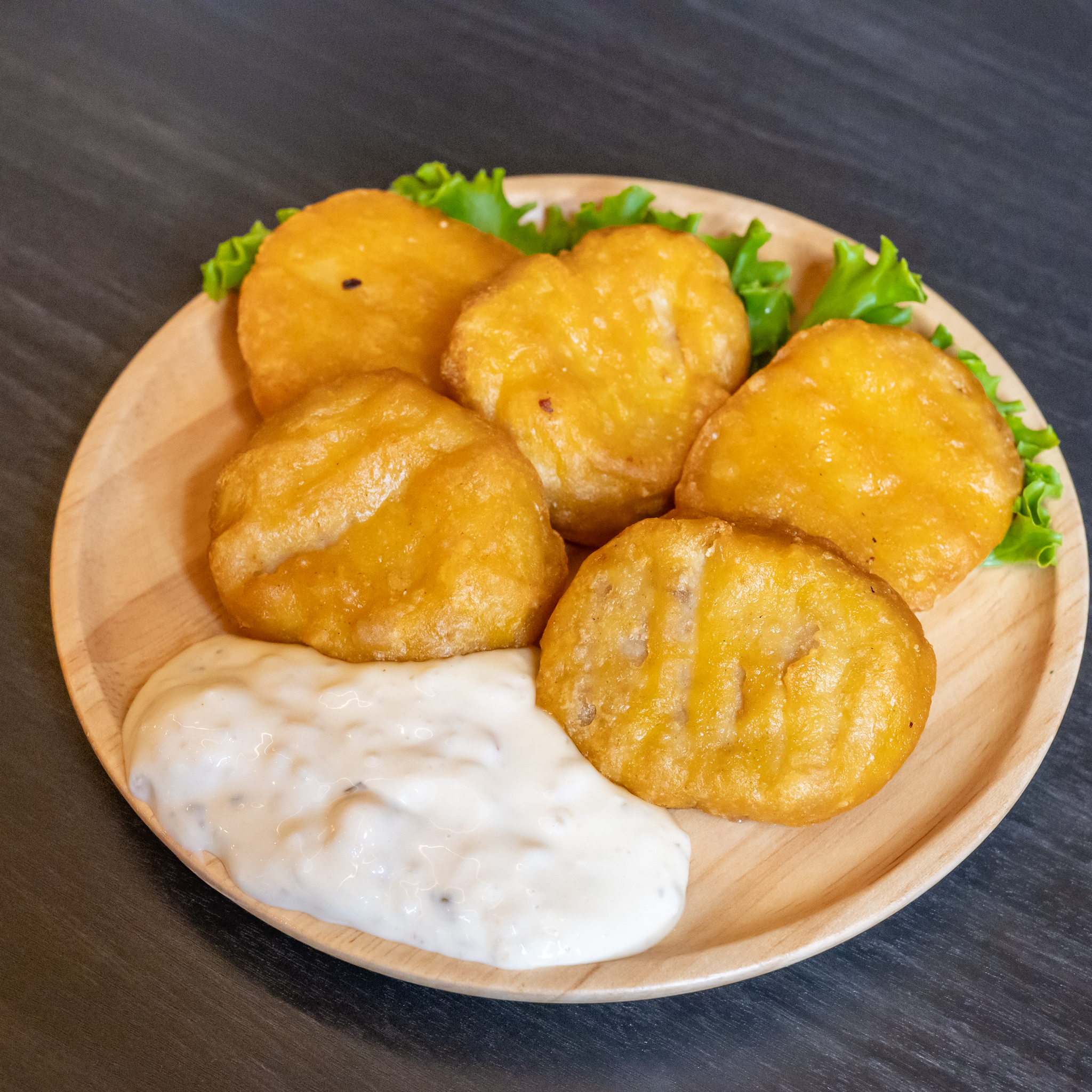 レタスを添えた木皿に盛られたチキンナゲットとタルタルソース