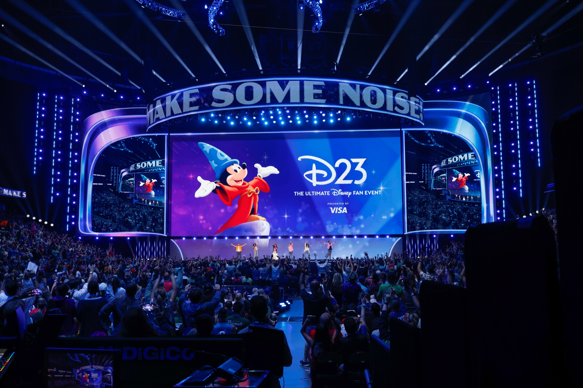 「MAKE SOME NOISE!」の看板と魔法使いのミッキーが映るスクリーン、手を挙げる客席