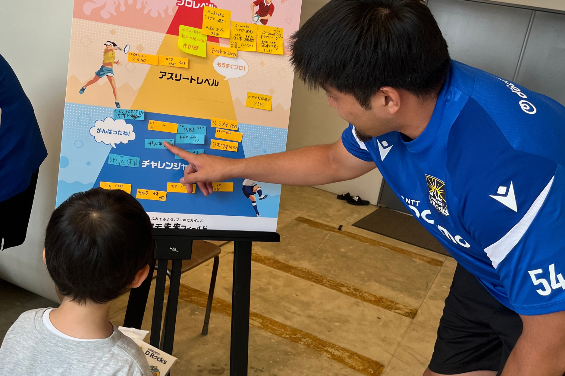 記録ボードを指しながらこどもに話しかける選手