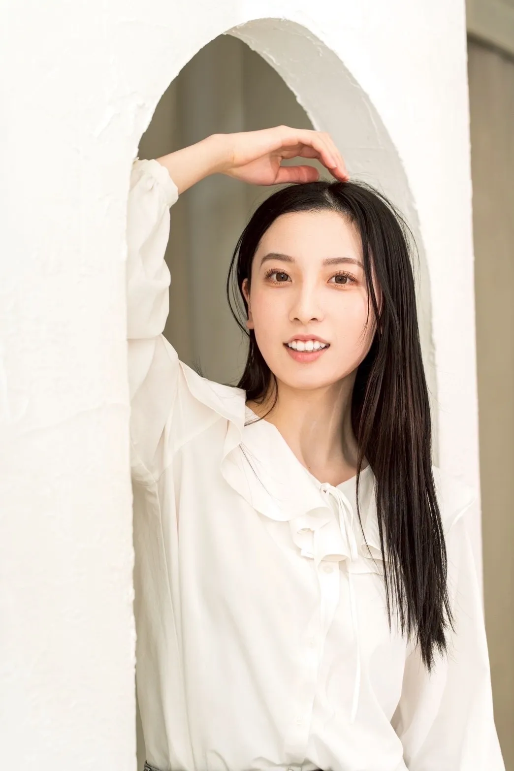 白いブラウス姿でアーチ型の壁の前に立つ出演キャスト