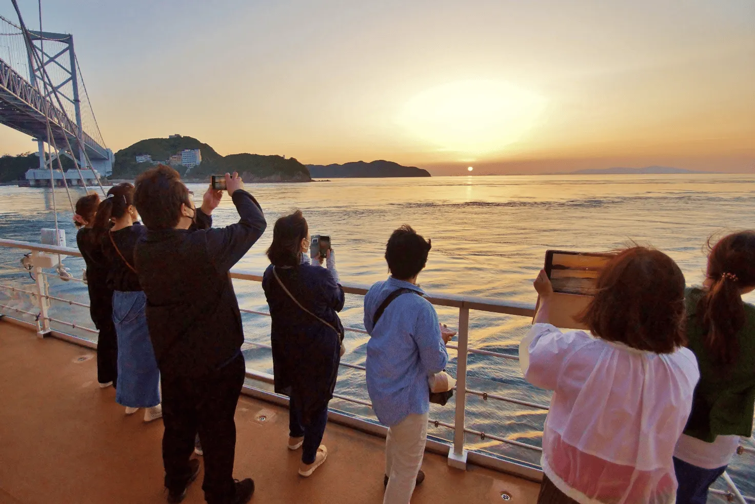 デッキから夕日を撮影する乗客たち