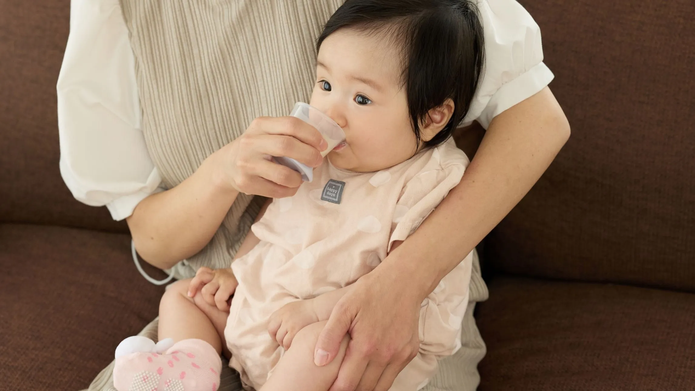 母親に抱かれ「はじめての練習コップ」で水分をとる赤ちゃん