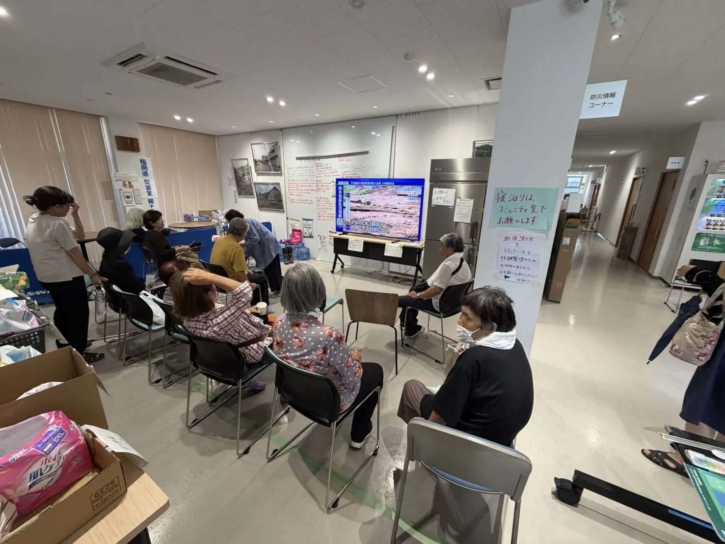 小川防災拠点センターのコミュニティ室でテレビを見る避難者