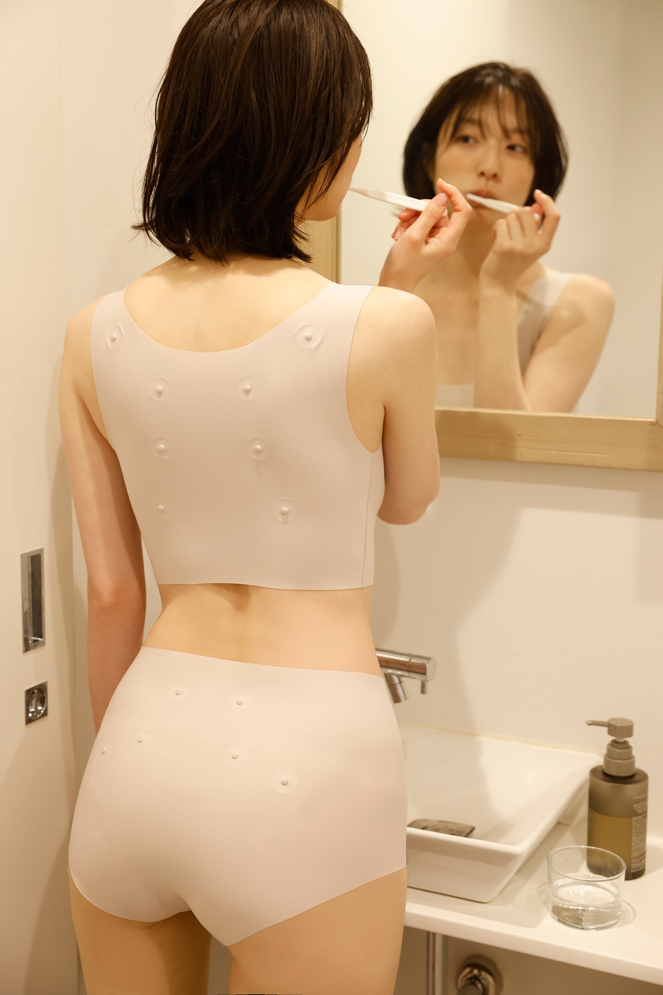 淡いピンクの「腰こりらっくす SEAMLESS」を着用し洗面台に立つ様子