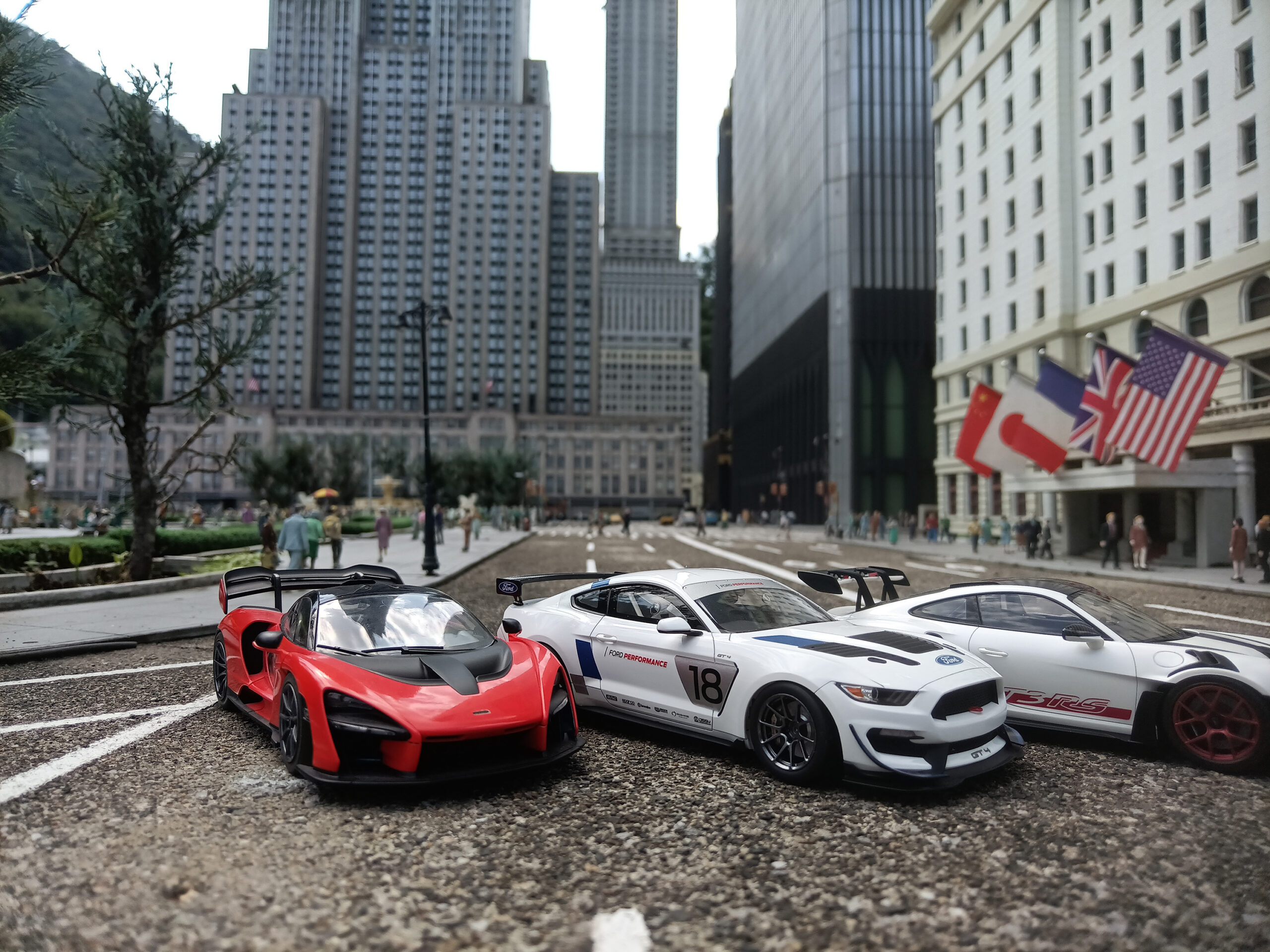 高層ビル群のミニチュアと各国の国旗を背景に3台のスケールモデルカーを並べた撮影例