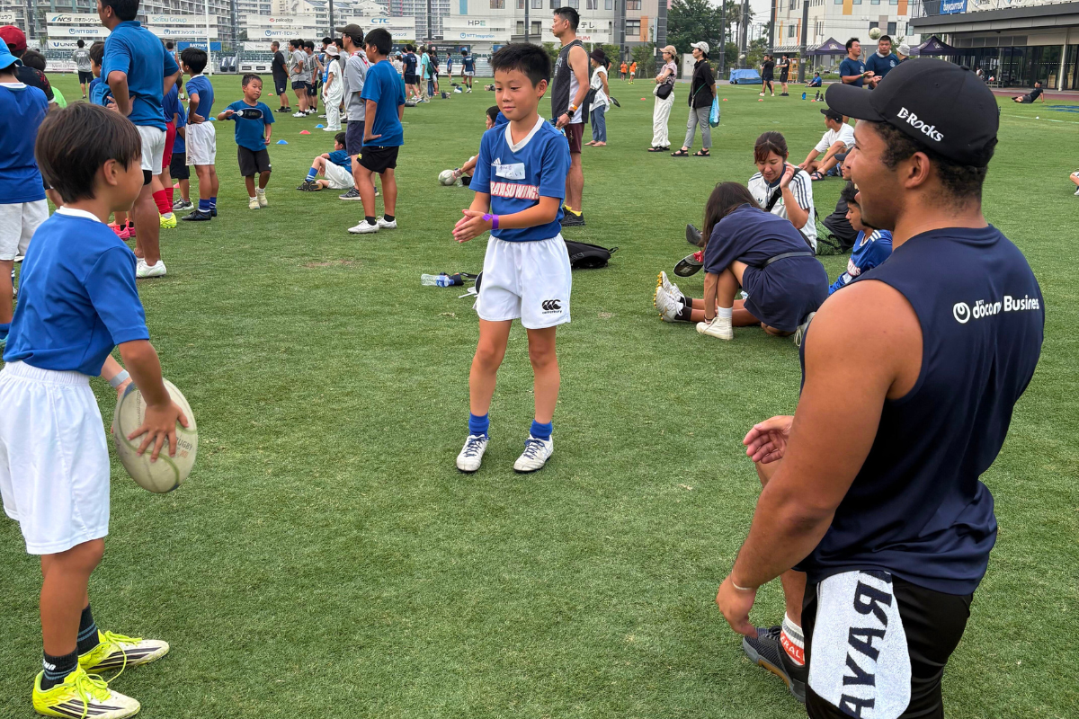ラグビーボールを持つこどもたちと見守る選手