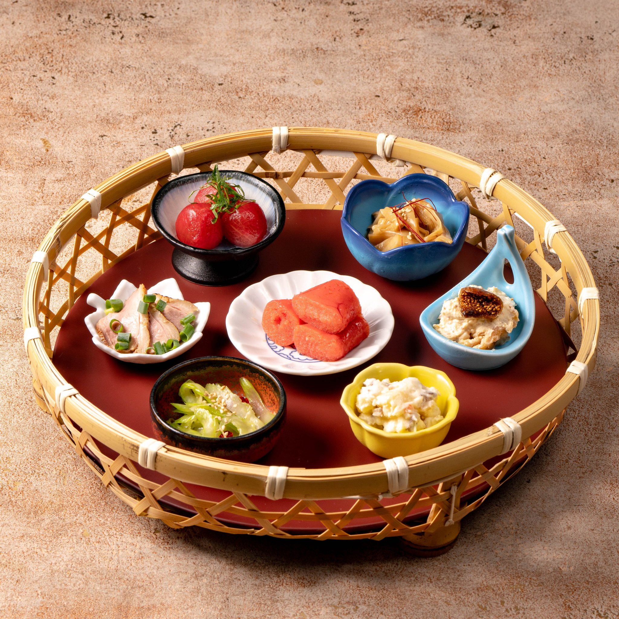 竹編みの盆に並ぶ7種の豆皿・小鉢のおばんざい七種盛り合わせ