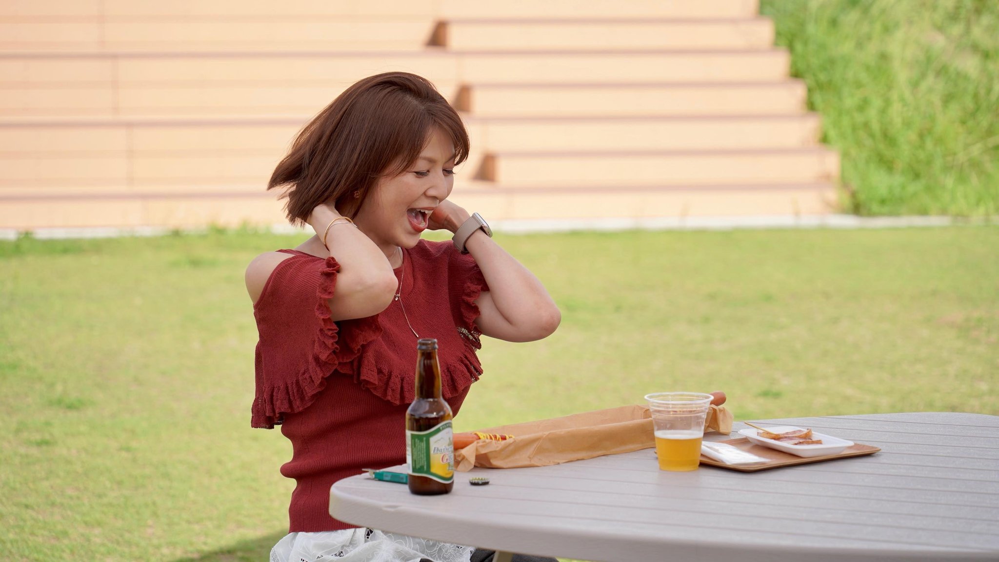 屋外のテーブルでビールと料理を前に笑う飯島直子