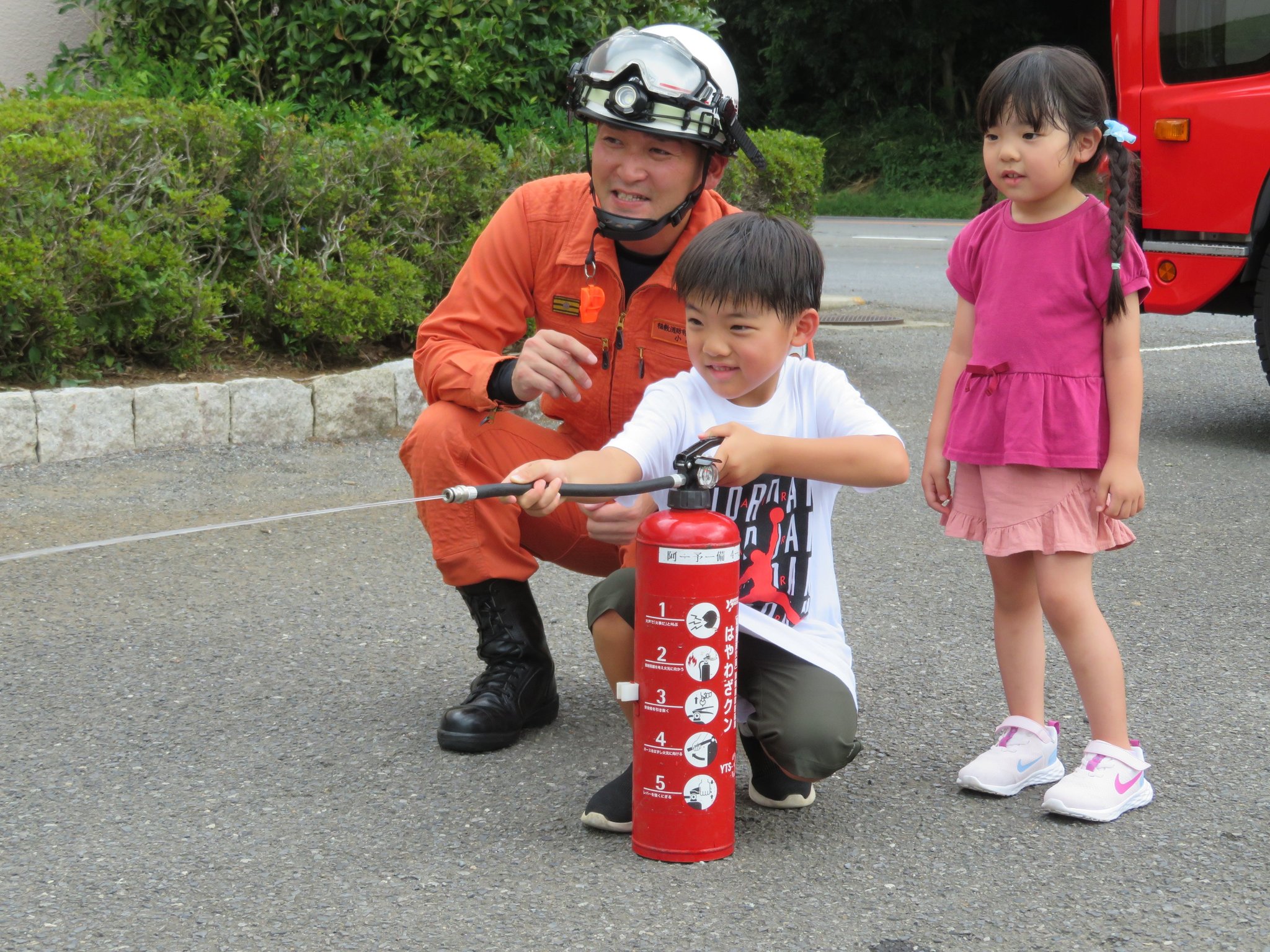 消火器体験会で消防隊員と子どもが水消火器を構える様子