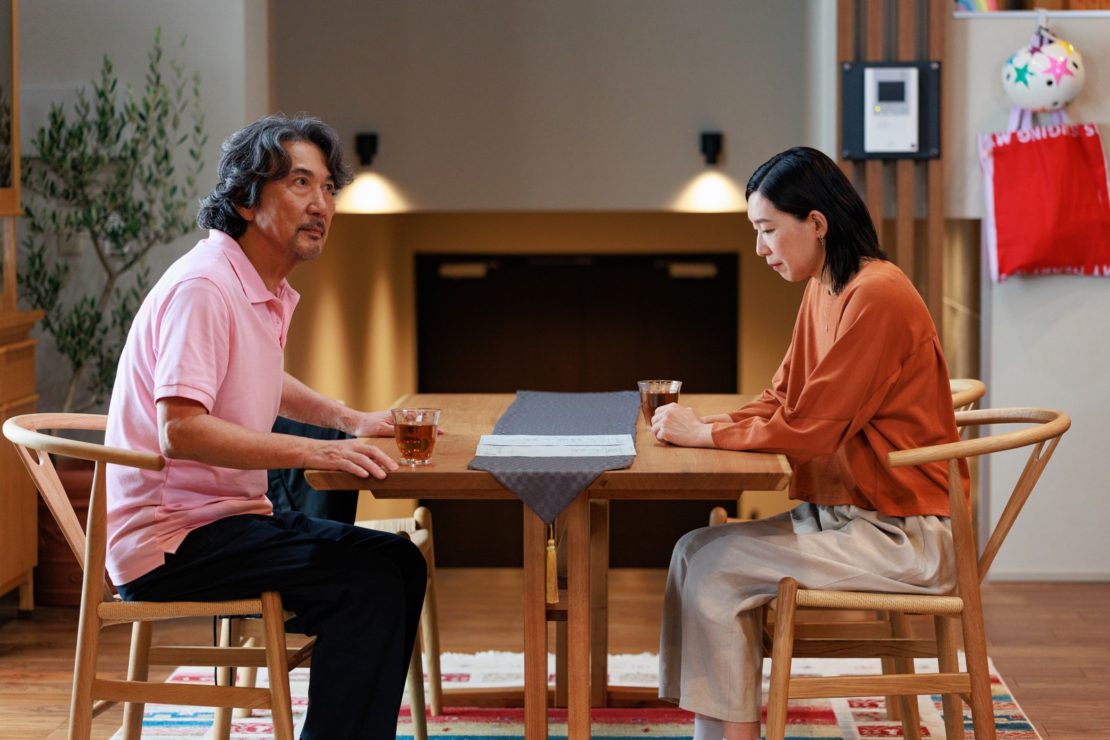 テーブルで向き合う高瀬川玄(役所広司)と女性の新場面写真