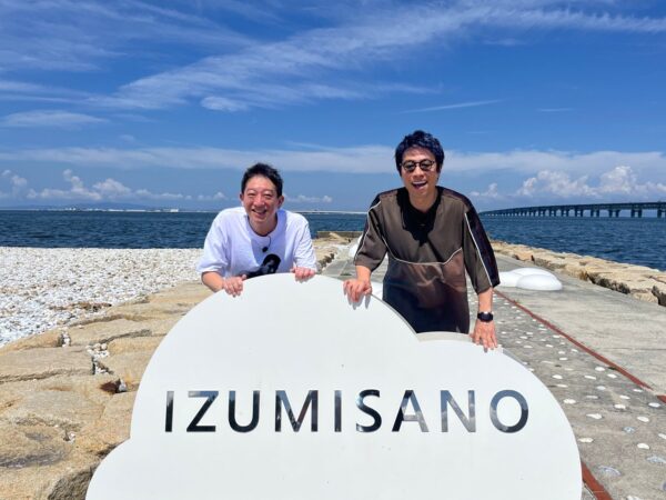 IZUMISANOの文字看板と2人