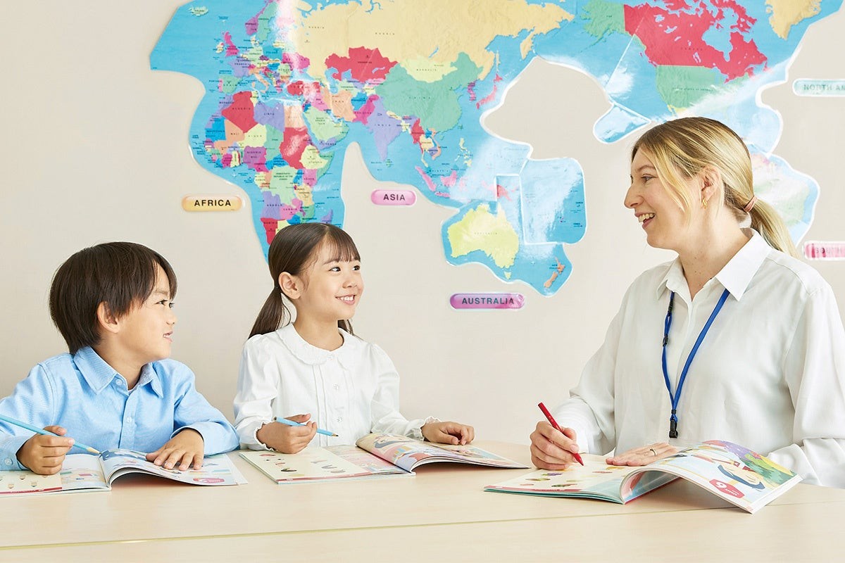 世界地図の前で講師と学ぶ子どもたちの様子