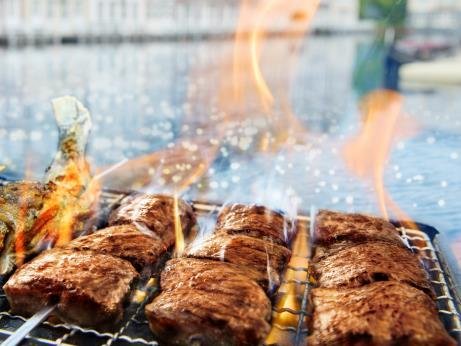 炭火焼きグリルで焼かれる肉と魚介の串焼き