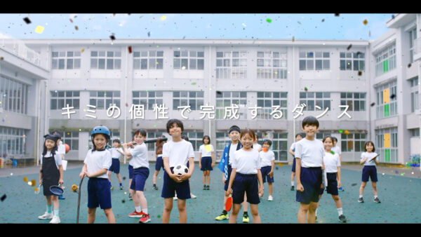 校庭に並ぶ子どもたちと「キミの個性で完成するダンス」のメッセージ