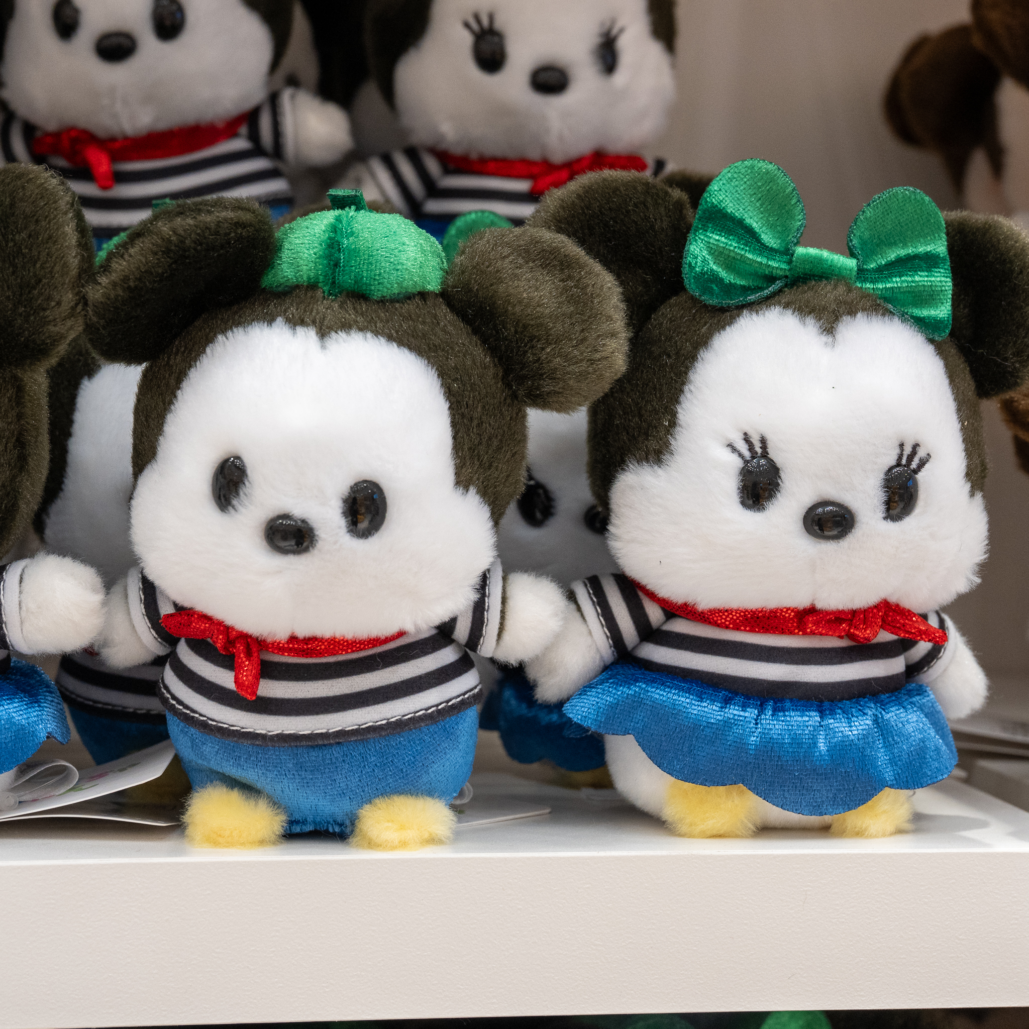 グリーンの帽子とリボンにボーダーの衣装を着た、丸いシルエットのミッキーマウスとミニーマウスのぬいぐるみ